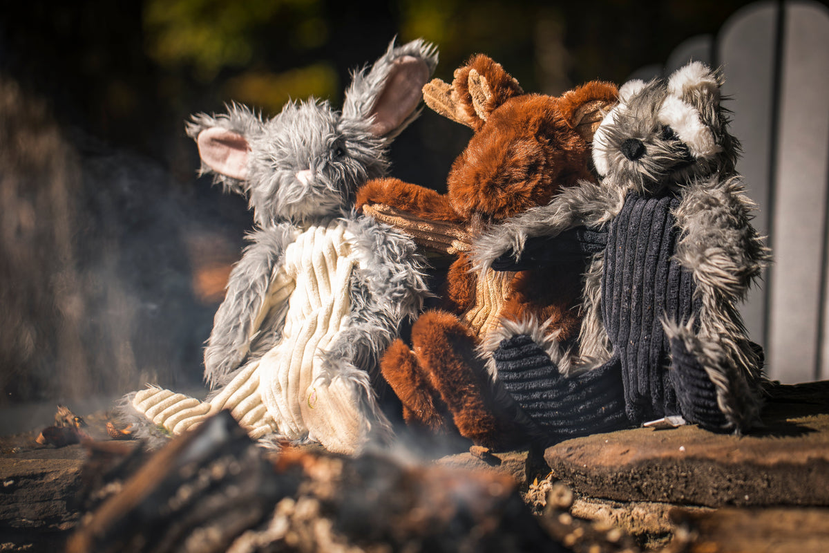 Plush dog toy in a raccoon design with gray fur, a white belly, and a dark ribbed body