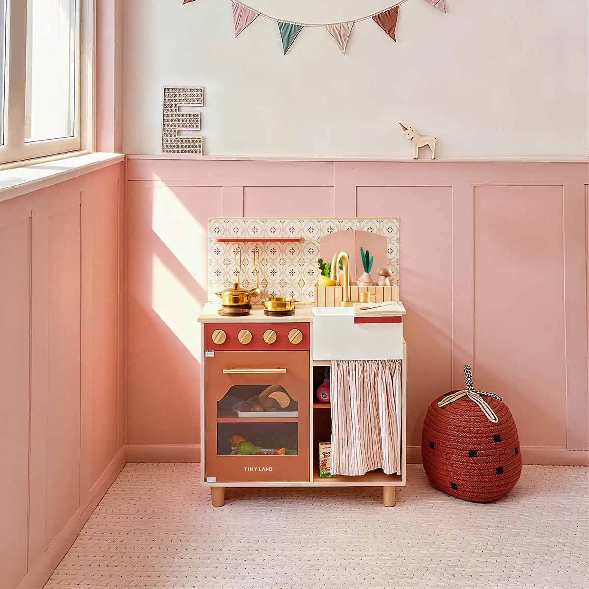 Tiny Land play kitchen with rust-colored oven, white sink, faucet, and striped storage curtain
