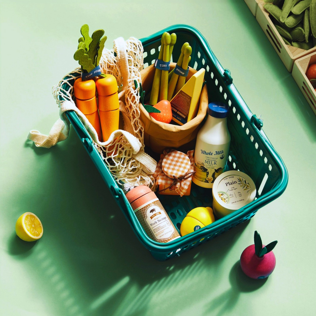 Teal shopping basket filled with toy fruit, vegetables, eggs, and milk cartons