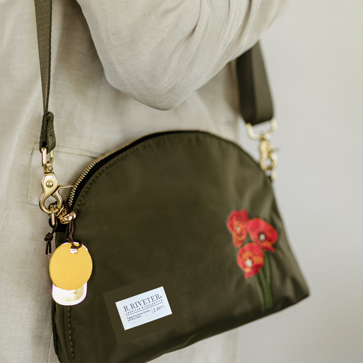 Olive nylon crossbody pouch on strap with red floral patch and zipper, gold clips