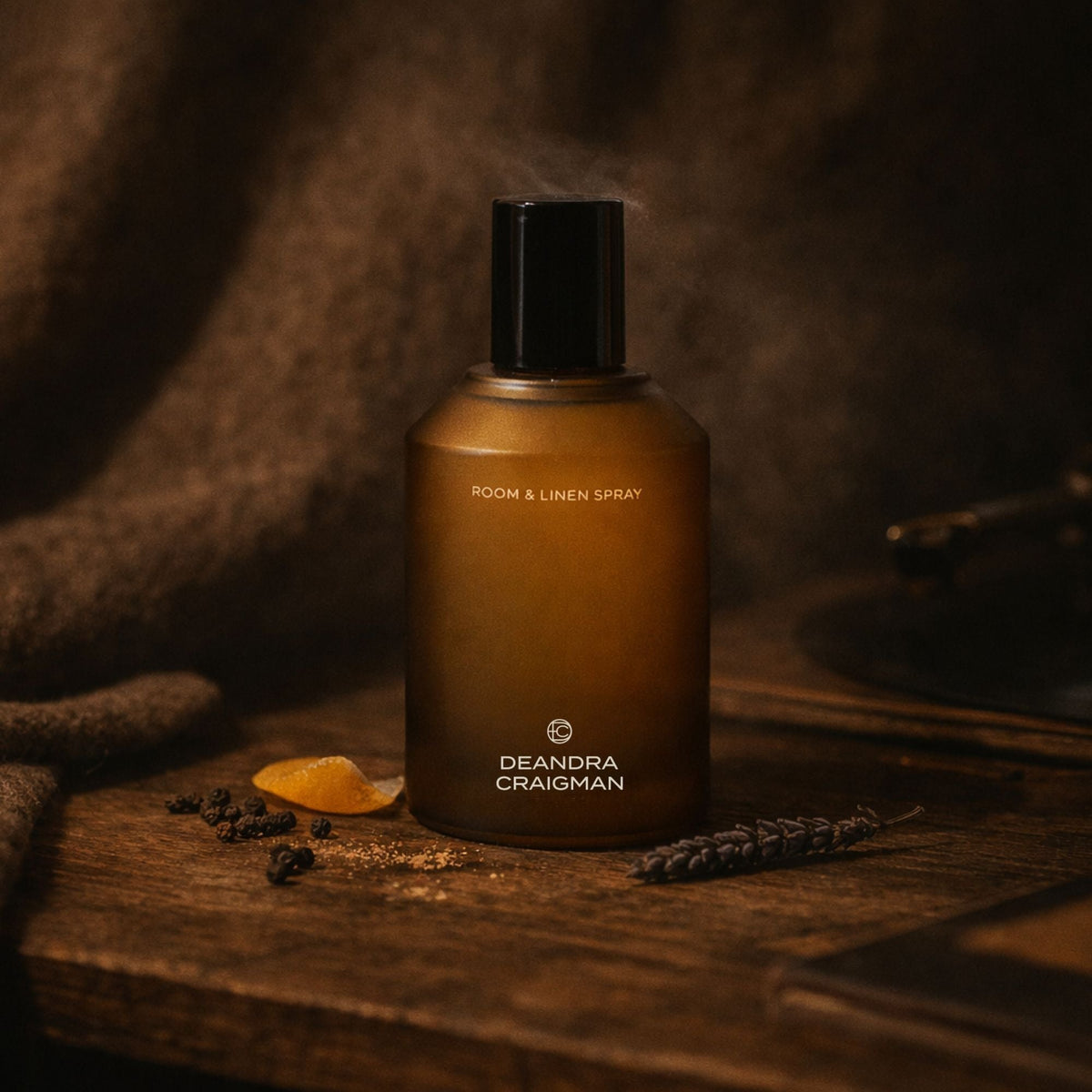 Amber room and linen spray bottle with black cap beside peppercorns