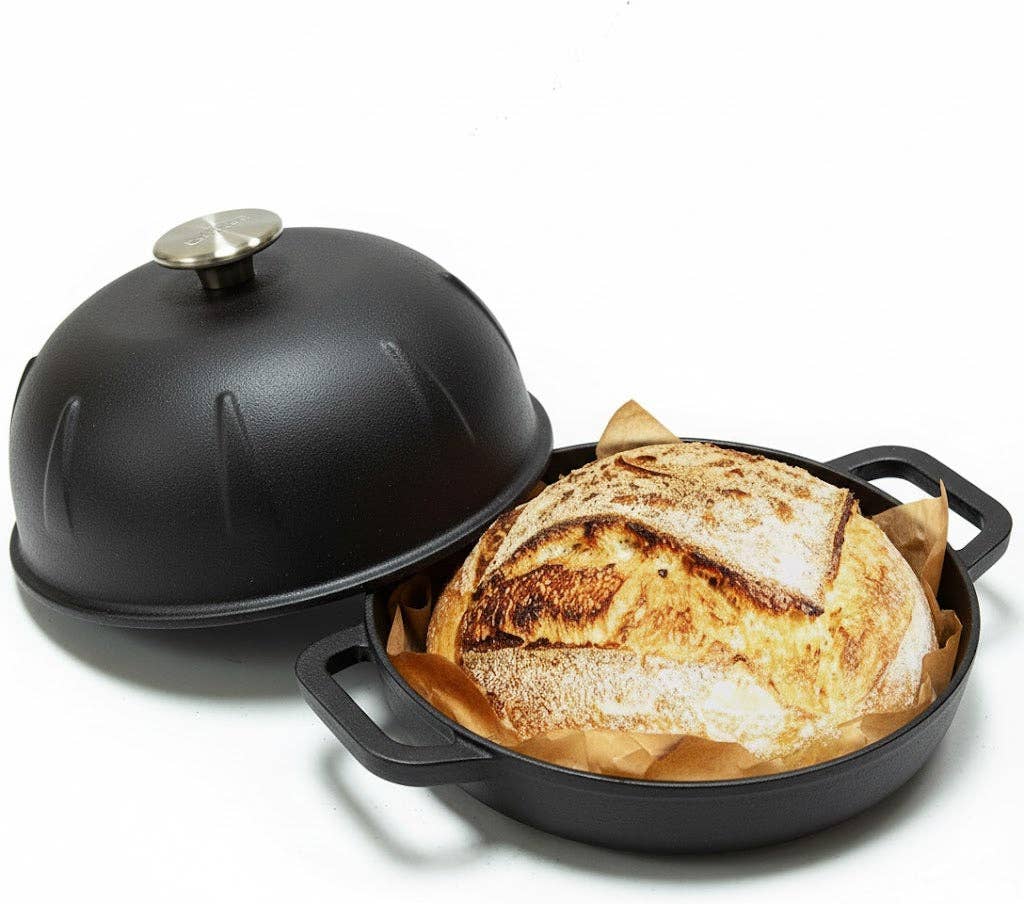 Black cast iron bread cloche with dome lid and loaf inside on base