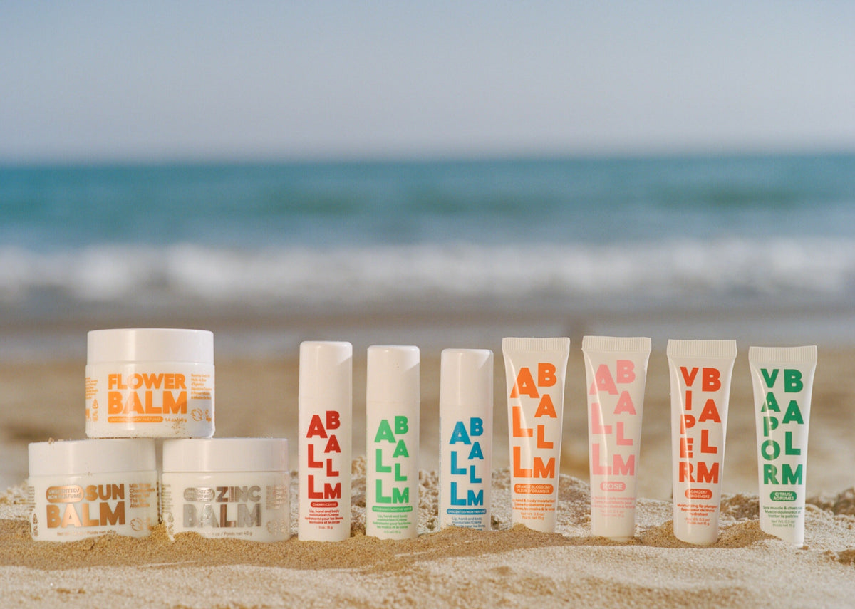 Assorted balm stick tubes lined up with visible caps on sand