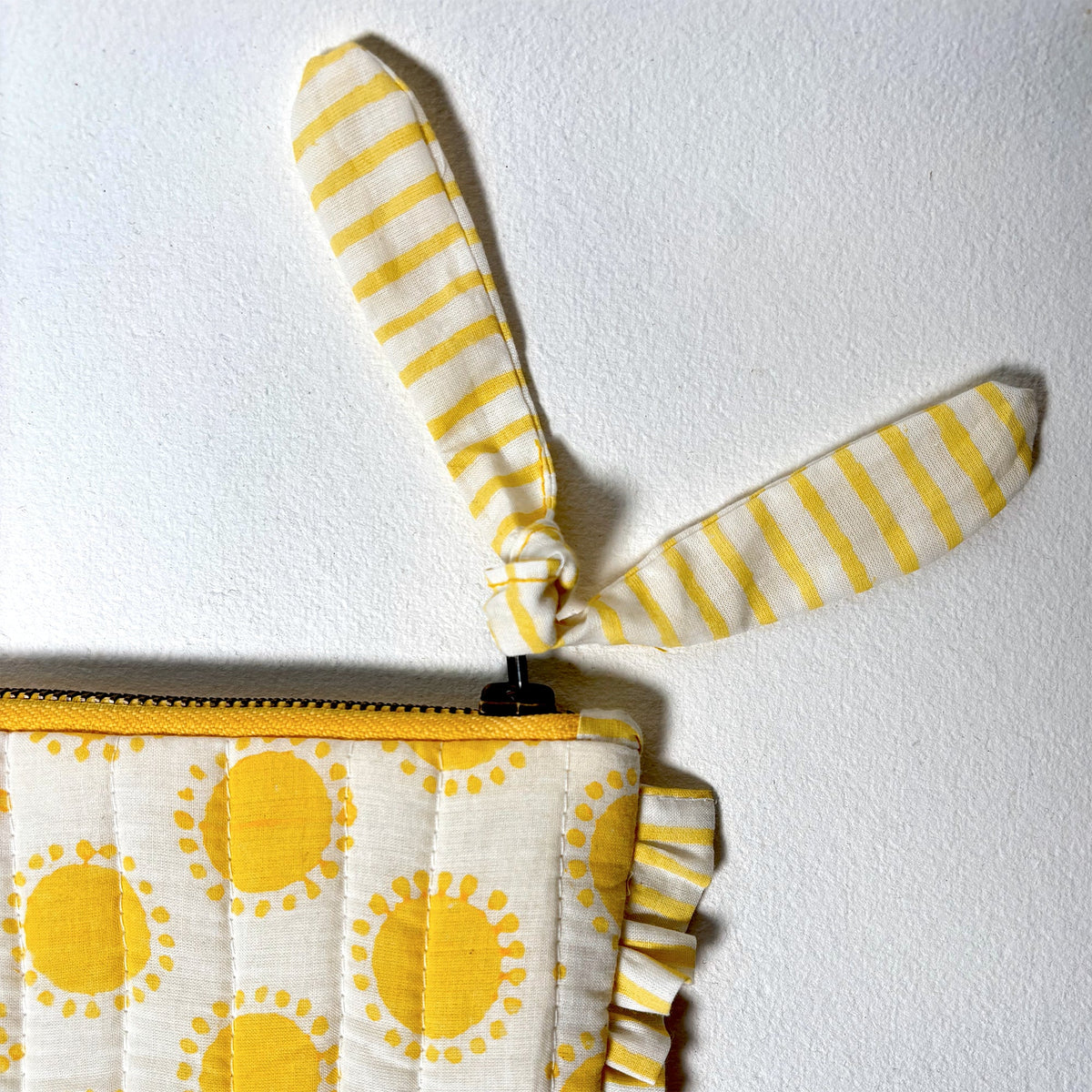 Close-up quilted pouch with yellow sun print, zipper, and striped handle pull