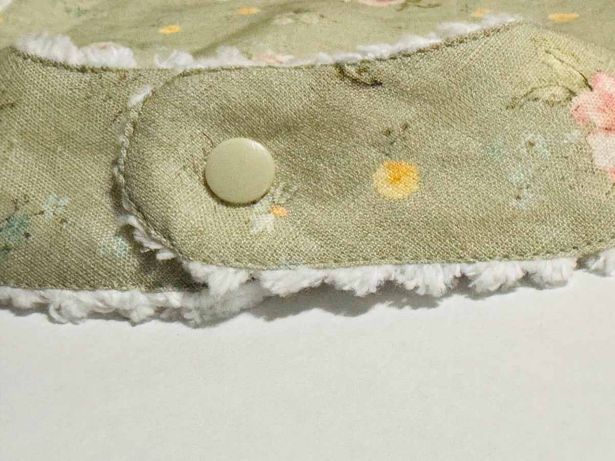 Infant bib close-up: sage floral tab with round snap button and stitched edge