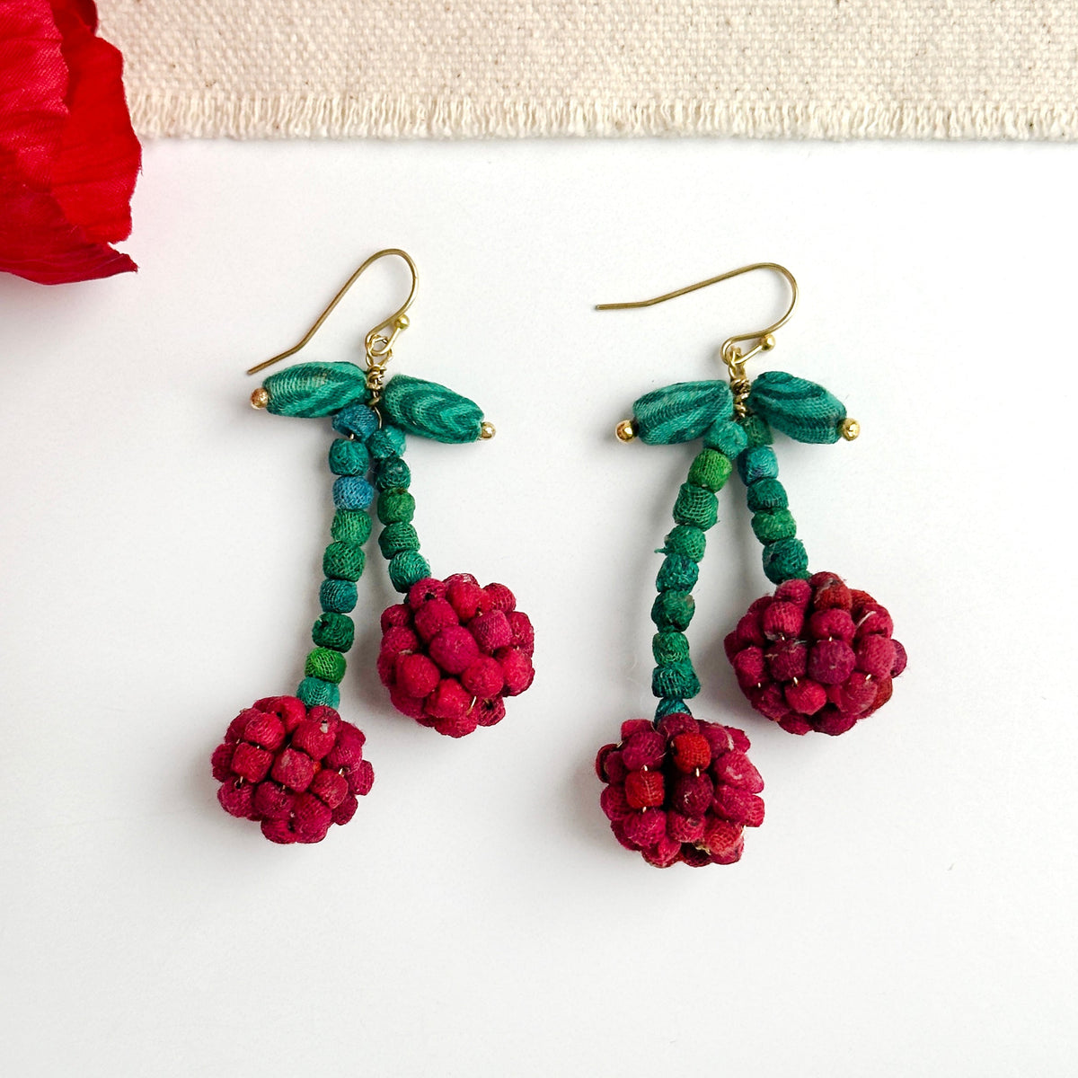 Teal and red beaded drop earrings, gold hooks, and berry pom-pom clusters.