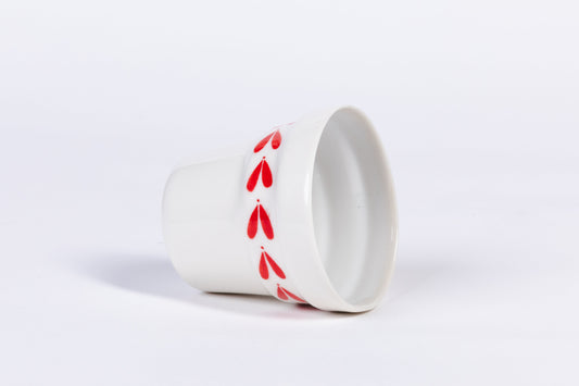 White ceramic espresso cup, side view with red leaf pattern near the rim