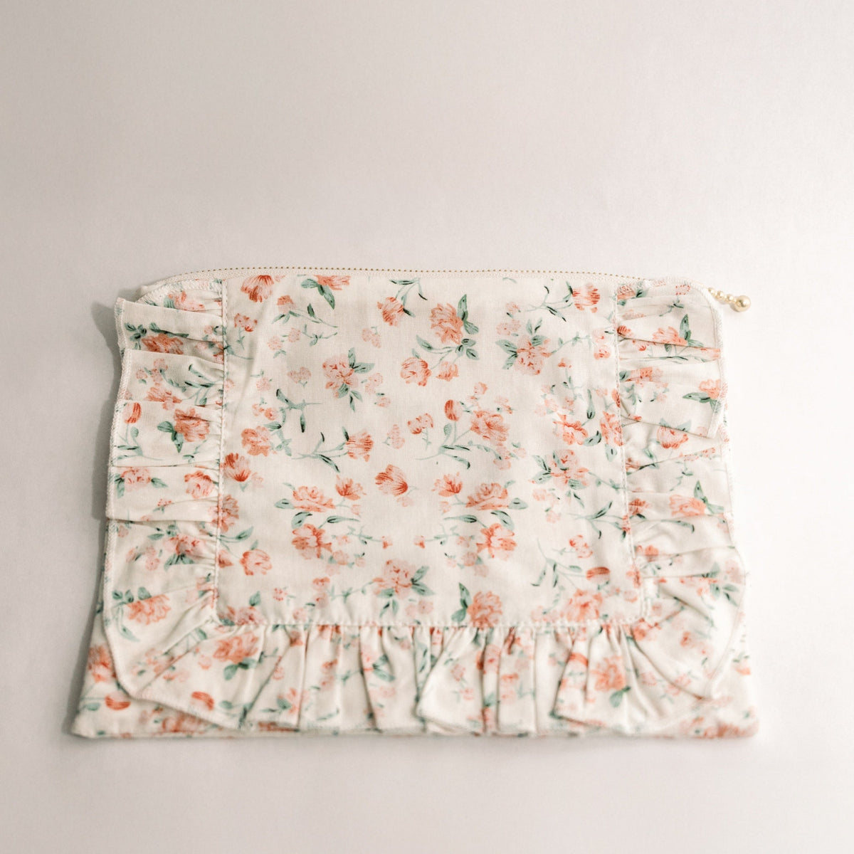 Floral ruffle zipper pouch in white with pastel blooms, gathered bottom ruffle, gold zipper pull