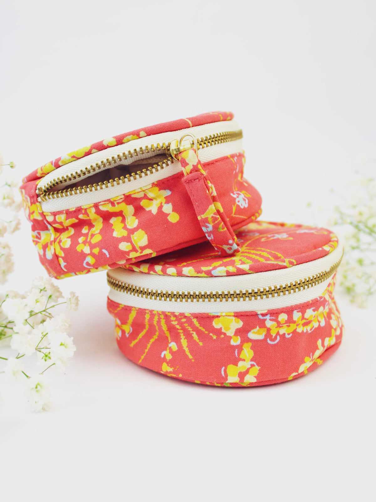 Stacked coral floral jewelry pouches with gold zipper openings and carry loop
