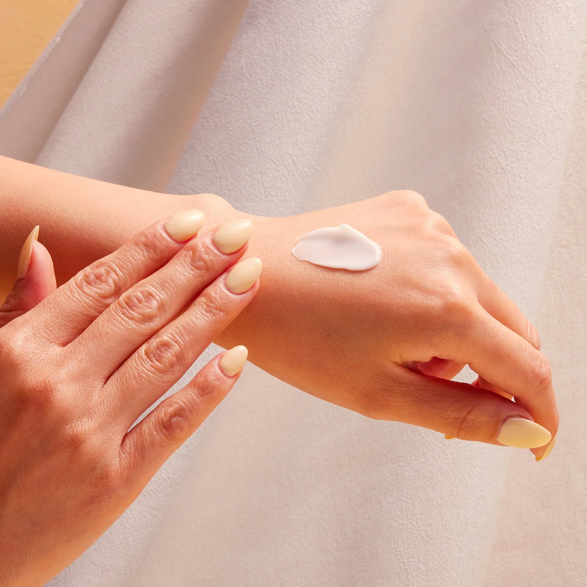 Hands applying a dollop of white hand cream to skin