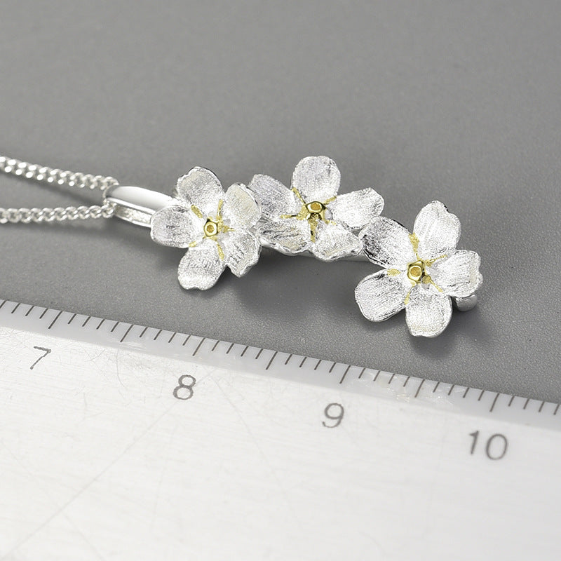 Silver forget-me-not flower necklace pendant with multiple blossoms laid near a ruler.