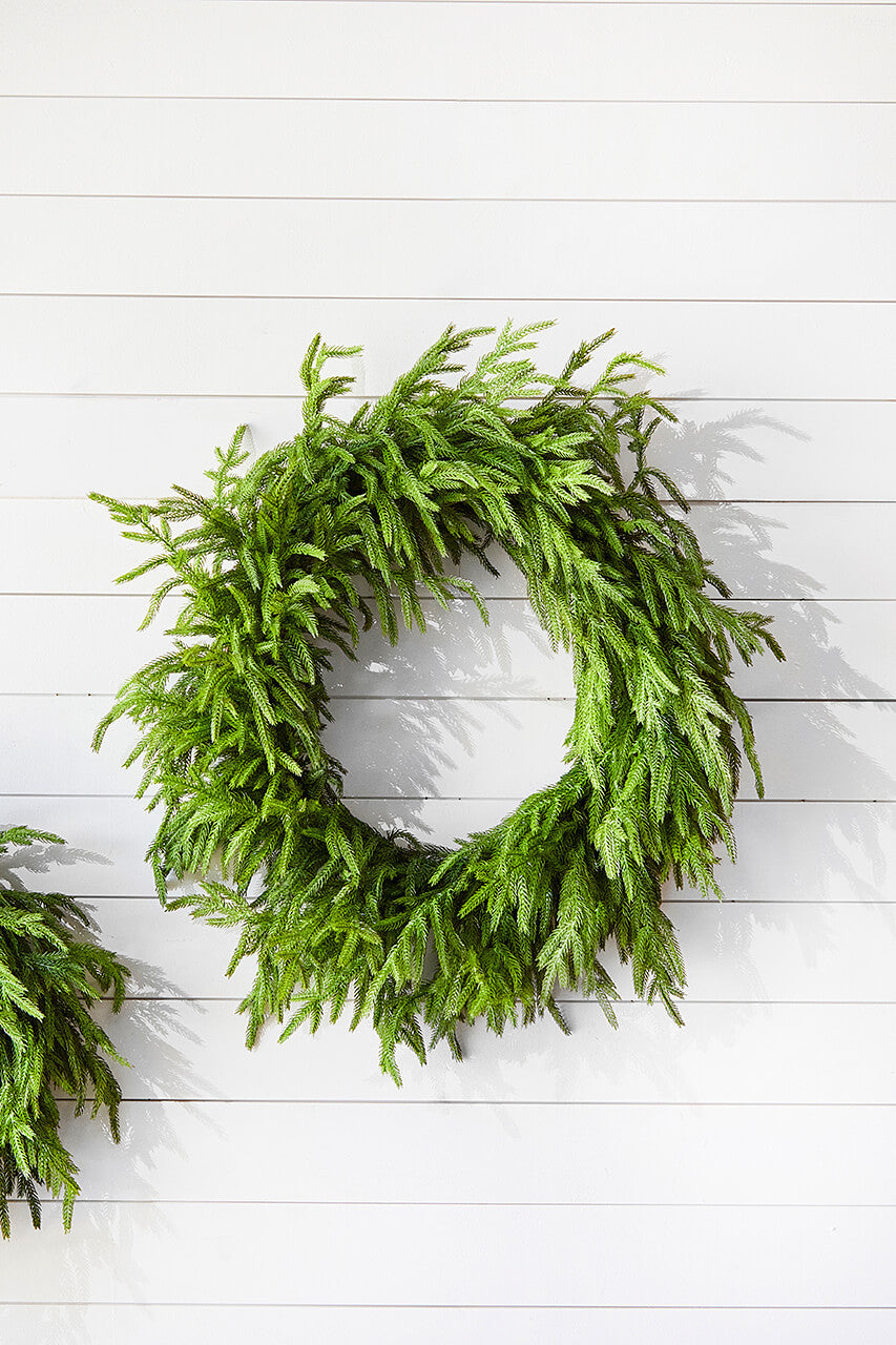 Green faux pine Christmas wreath against a white wall with horizontal boards.