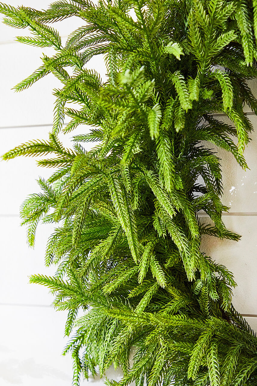 Green faux pine wreath with full, layered fronds and dense needle texture.