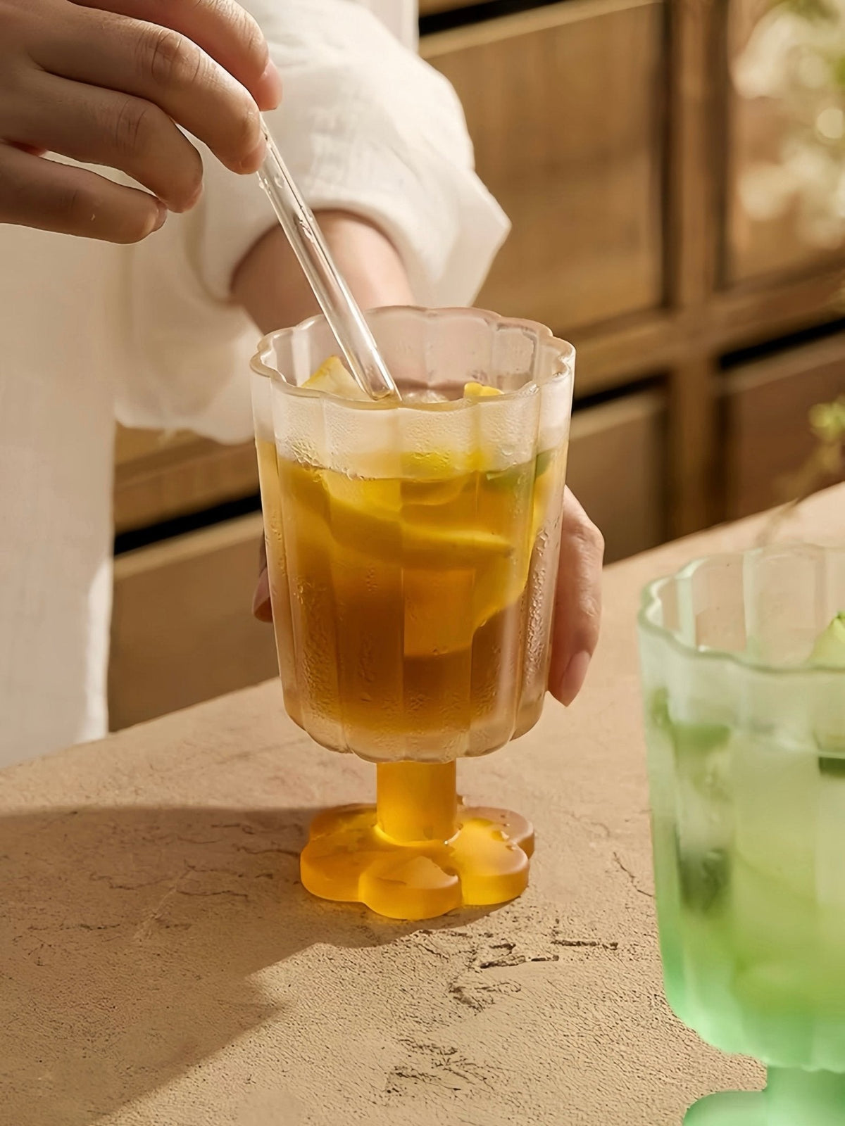 Hand-blown petal goblet glass with amber drink, on yellow stem and flared base.