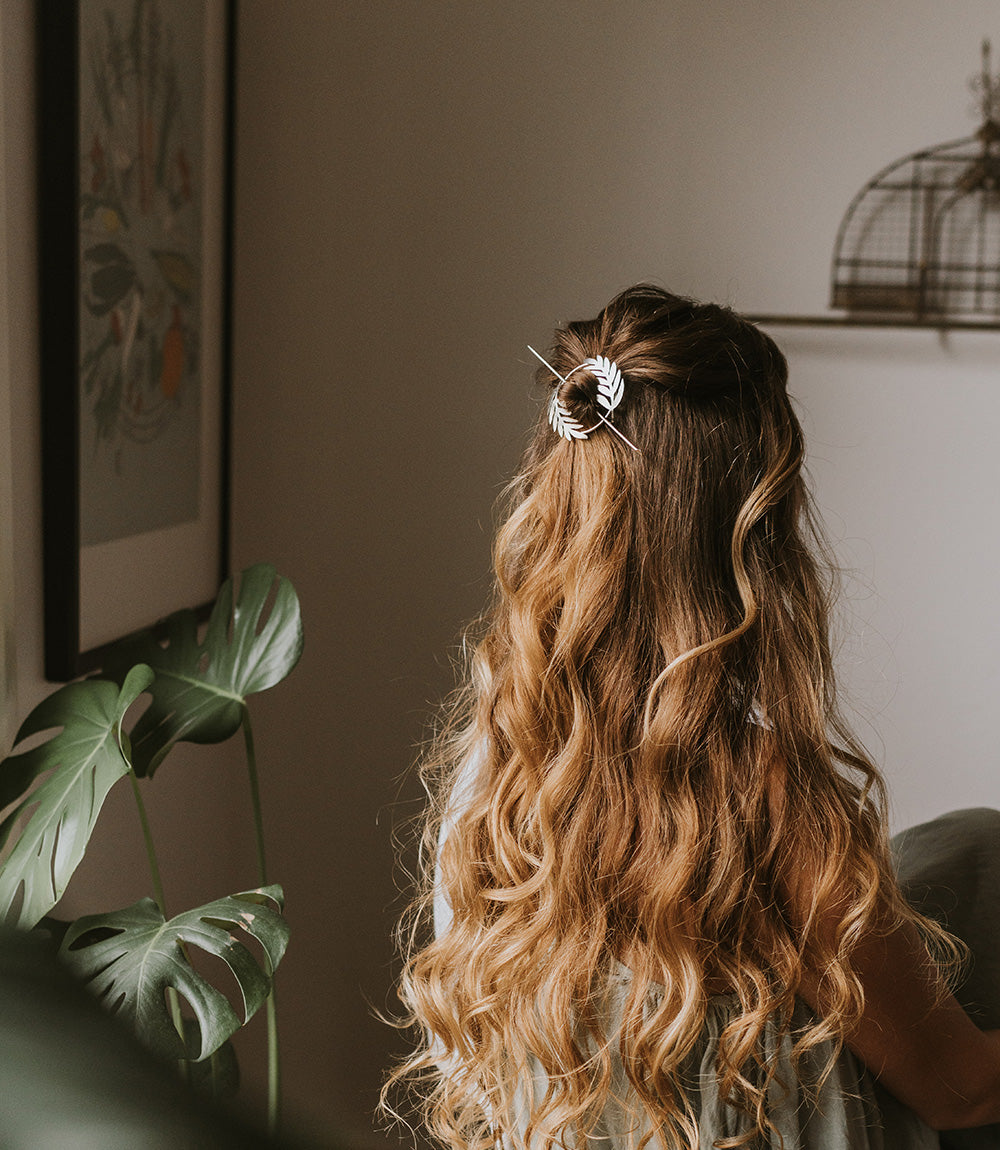 Silver fern hair slide clipped into long wavy hair with fern leaf accents.