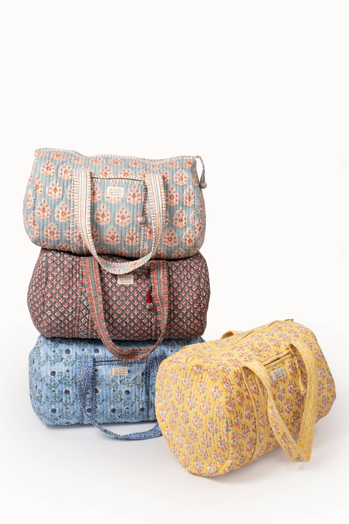 Assorted quilted block print duffle bags in blue, rust, and yellow with zipper closures