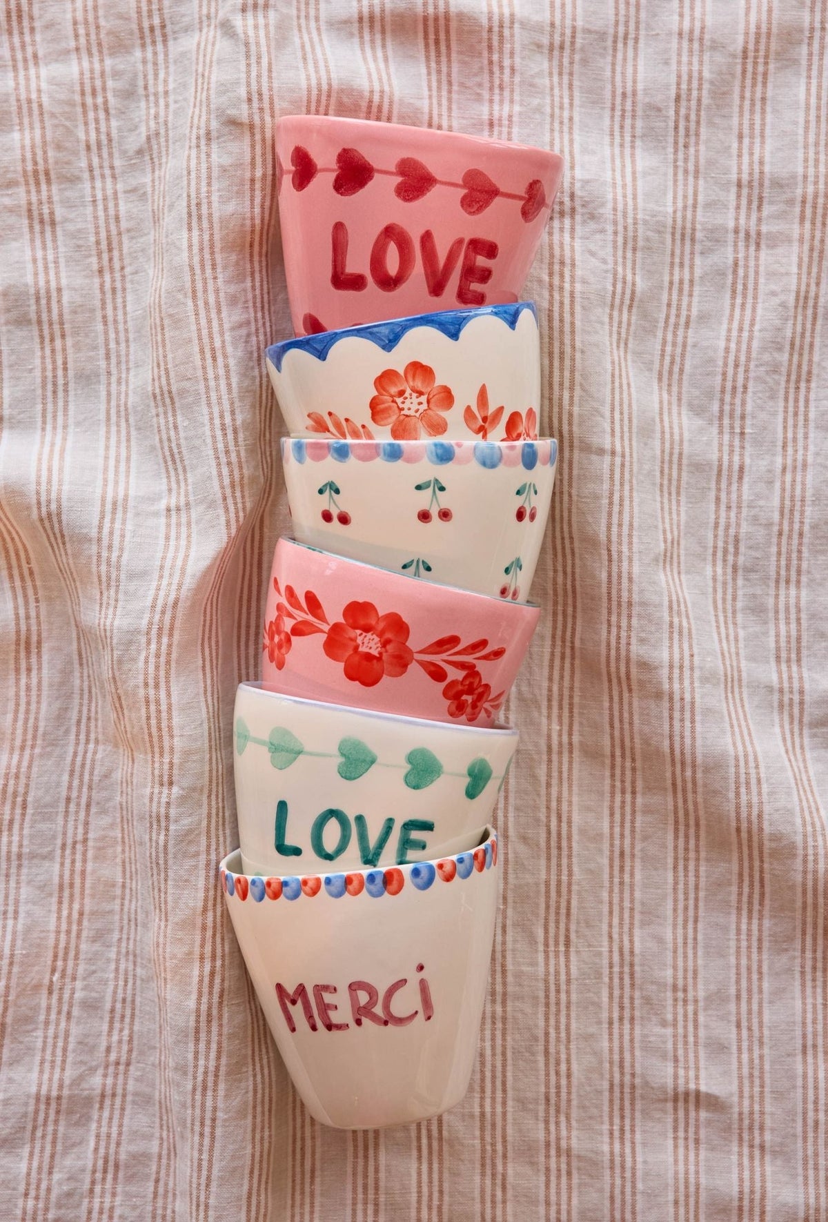 Set of ceramic cups with hand-painted Love and Merci designs, stacked.
