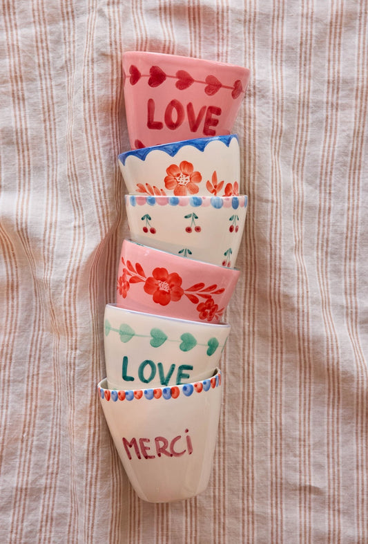Set of ceramic cups with hand-painted Love and Merci designs, stacked.