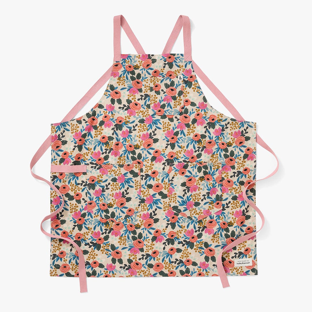 Floral crossback apron with pink straps and front pocket on natural fabric.