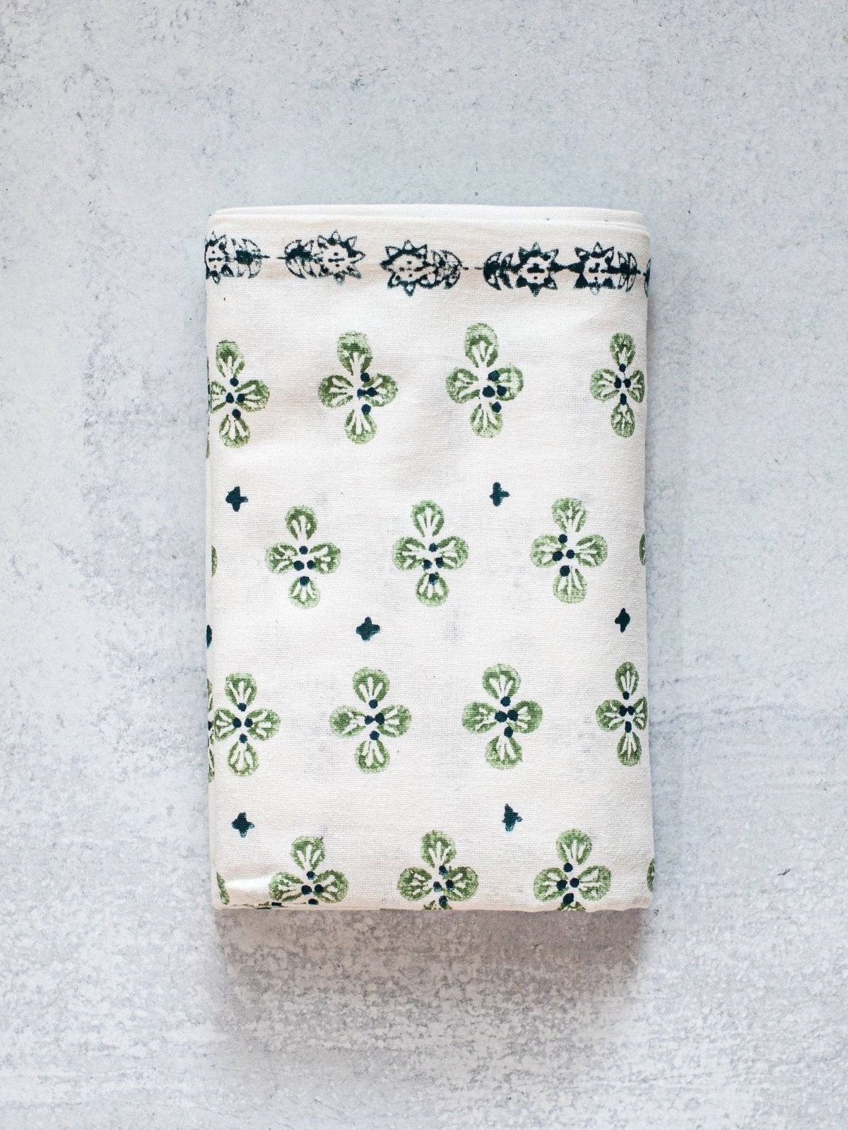 Ivory table throw with green clover print and dark blue striped border, folded