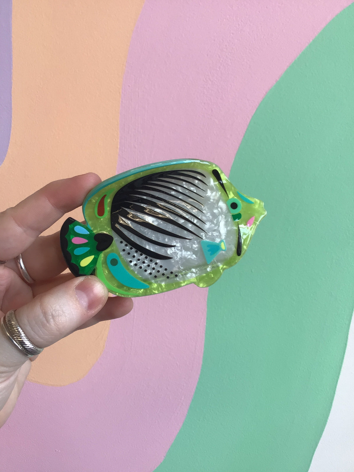 Green fish-shaped hair claw with black-and-white ribbed center and multicolor accents