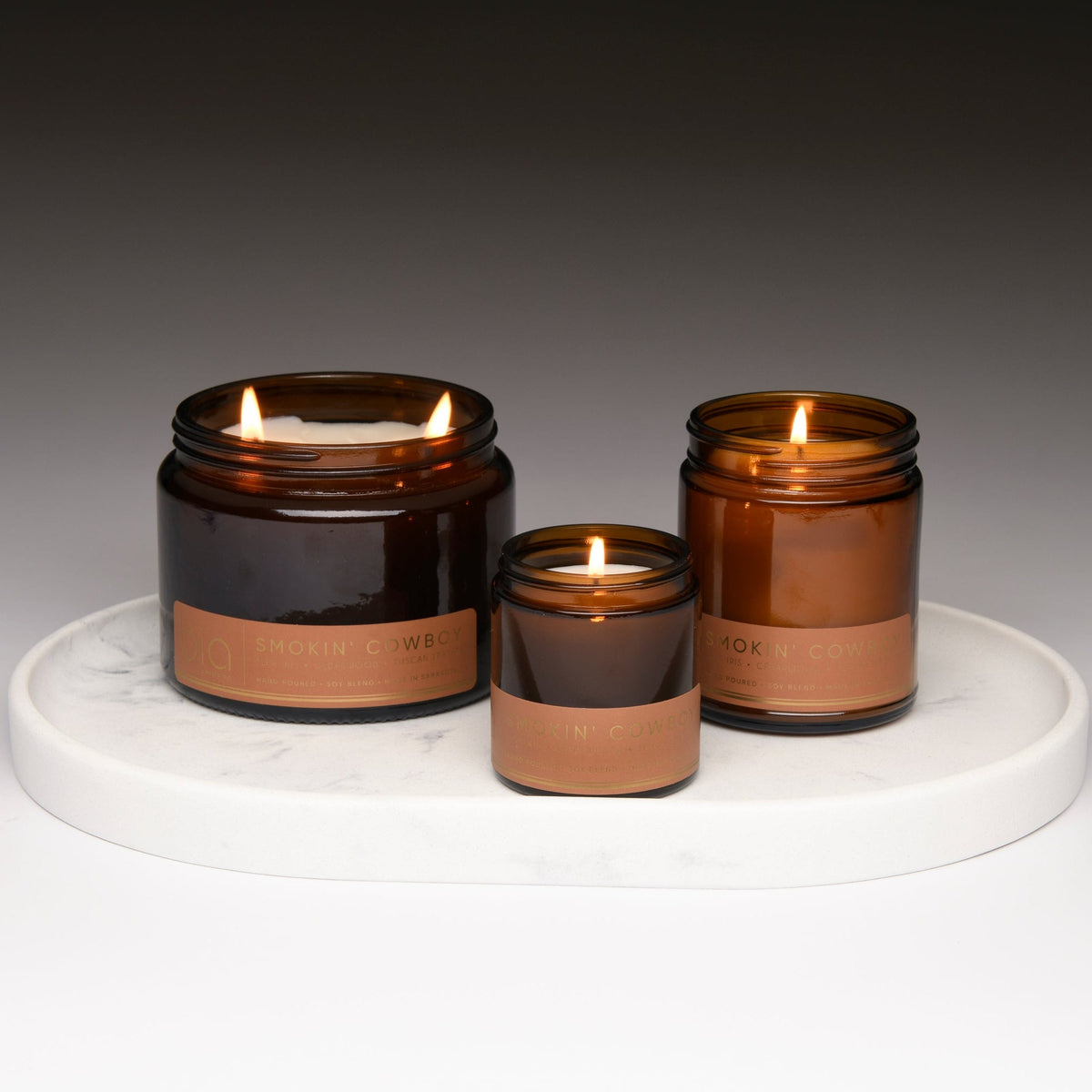 Three amber soy candle jars with lit flames on a round white tray