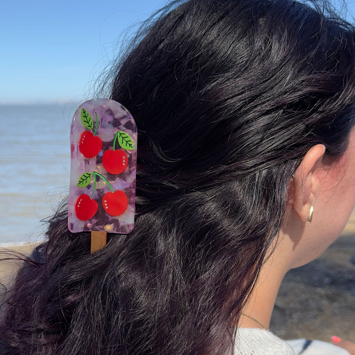 Cherry popsicle hair claw on dark hair with translucent pink body and red cherry print