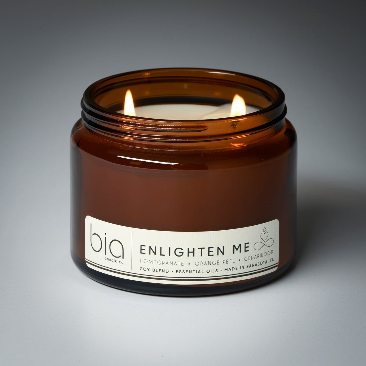 Amber glass jar candle with two flames and white ENLIGHTEN ME label