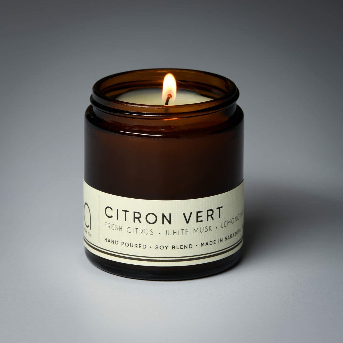 Close-up of lit amber soy candle jar with label around jar