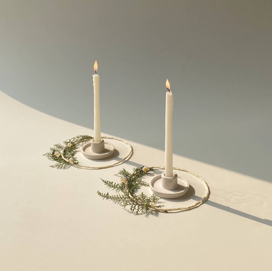 Pair of white ceramic candle holders with two lit taper candles and greenery