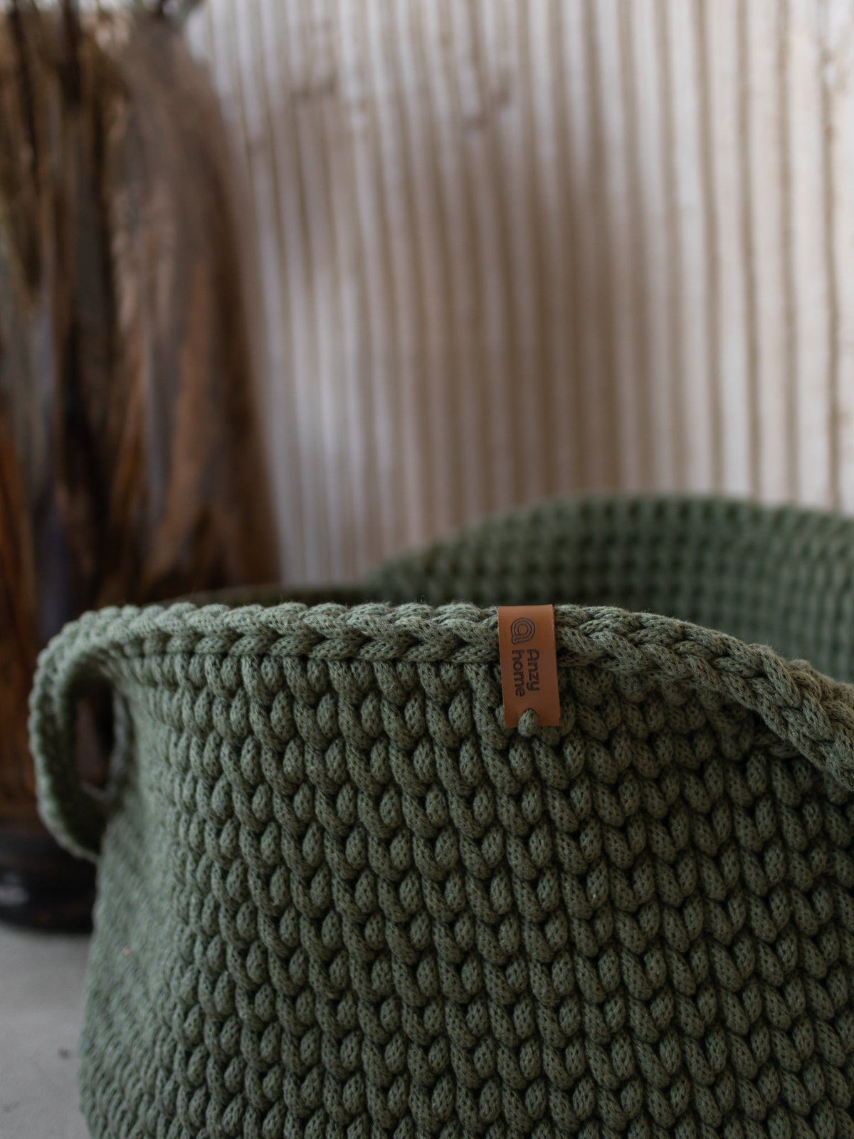 Round woven basket with handles, close-up of olive-green weave and tag.