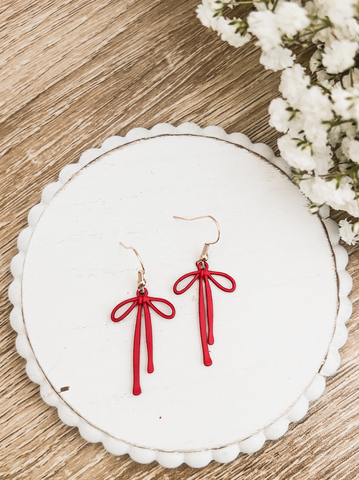 Red bow drop earrings with hanging tassel strands and gold-tone hooks on white card
