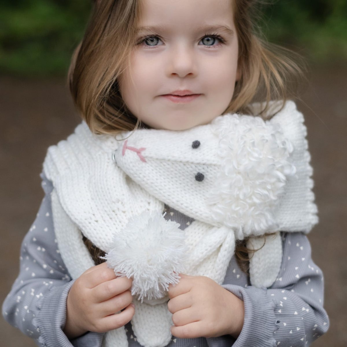 Child wearing a white knitted lamb scarf with a fluffy pom-pom and lamb face