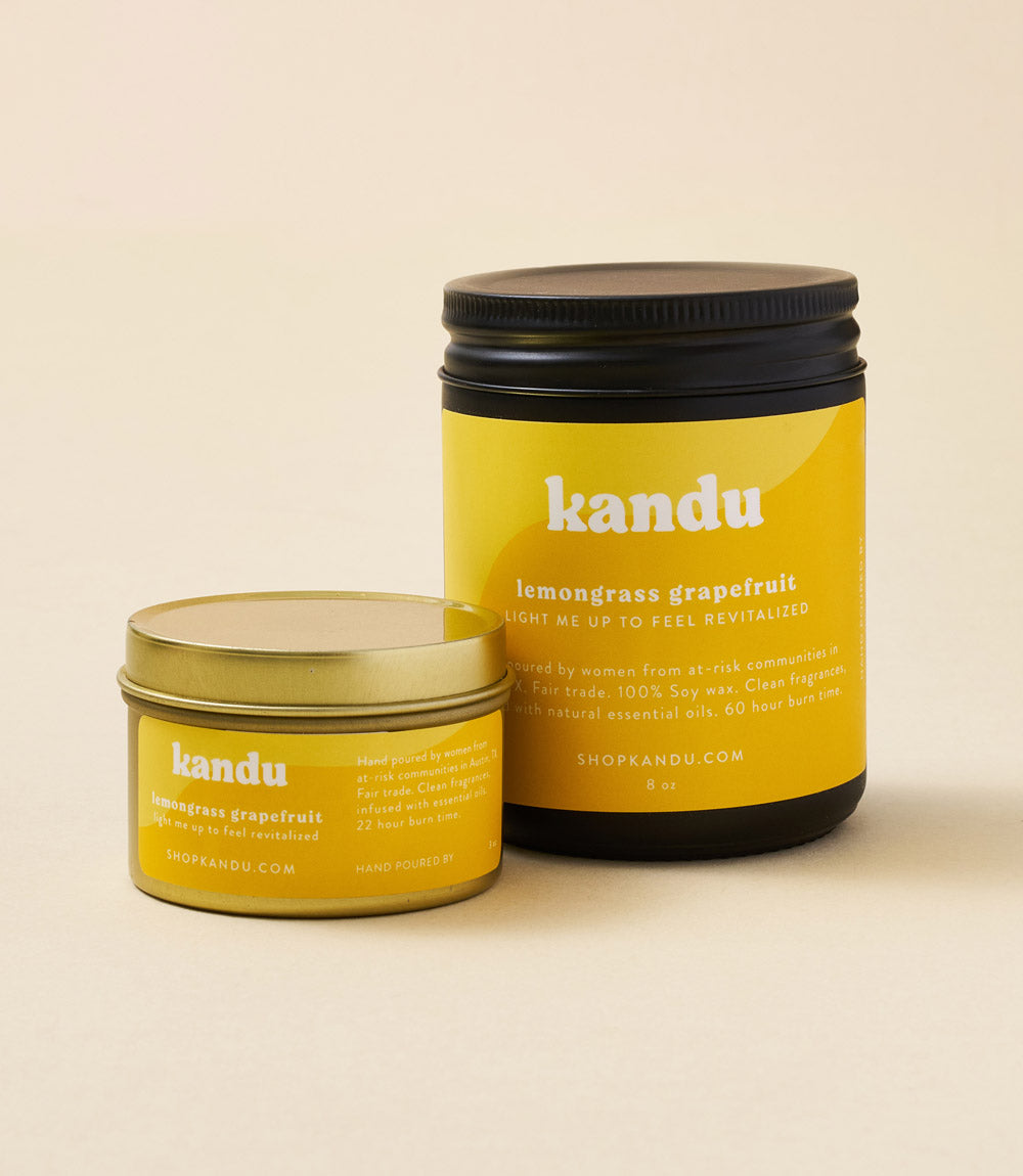 Two yellow kandu candle jars with black lids; smaller jar lid open, front label facing forward.