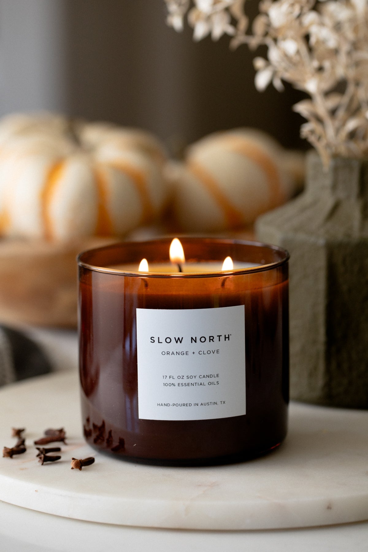 Orange clove 3-wick candle in amber glass jar on a white tray, flames lit