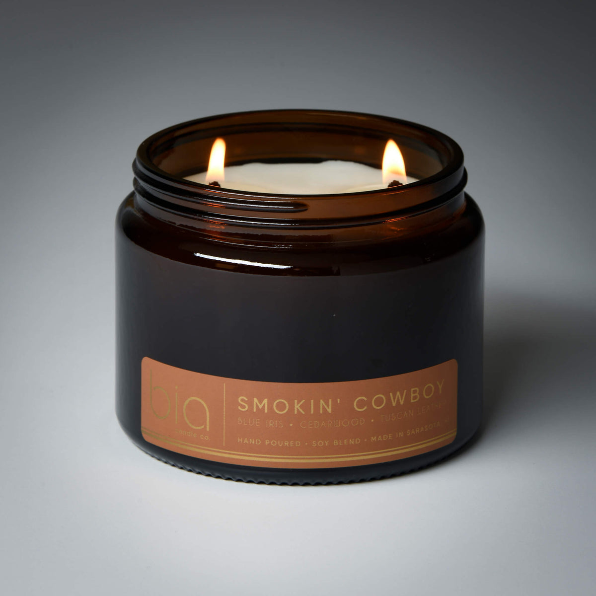 Dark glass candle jar with two burning flames and 'Smokin' Cowboy' label