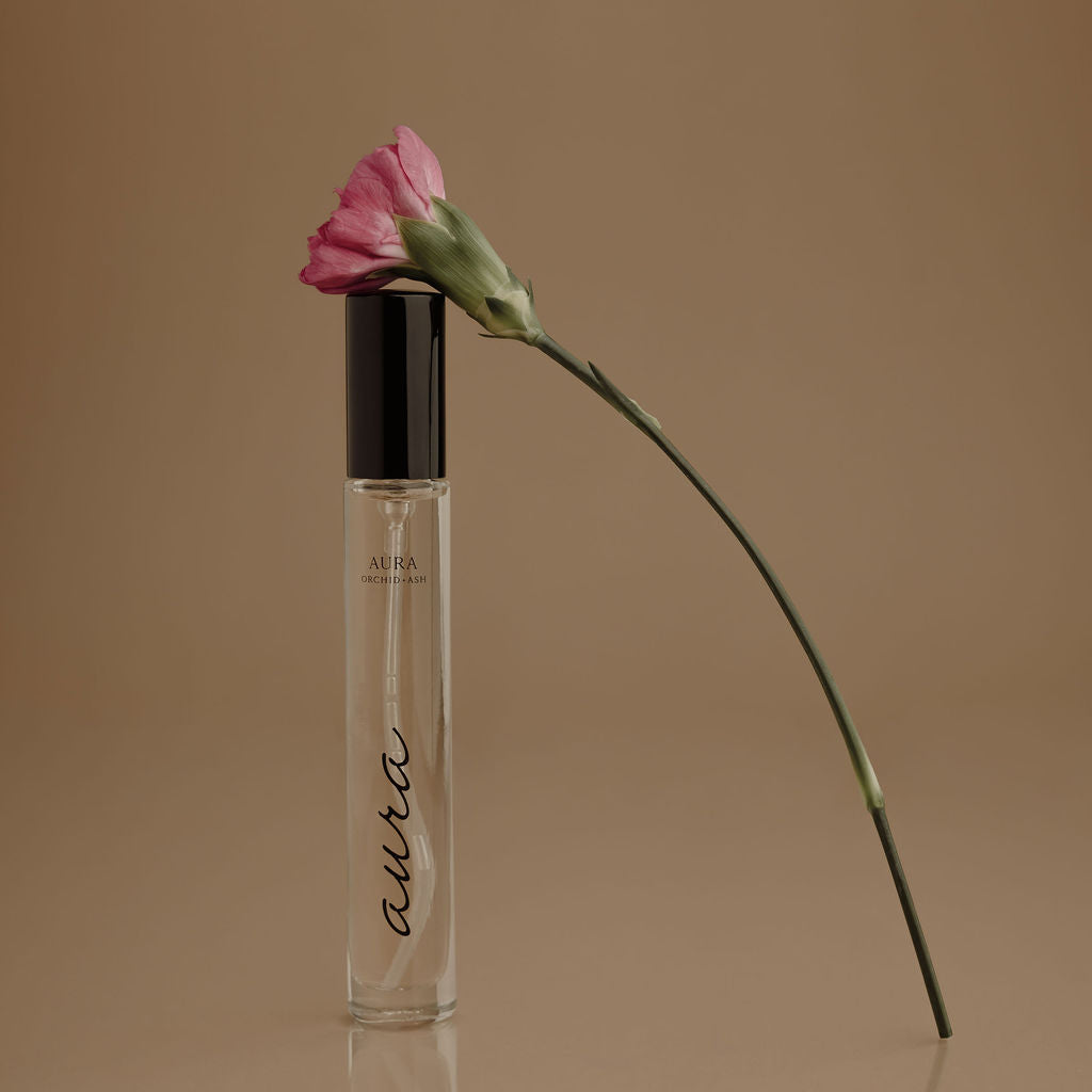 AURA perfume travel spray bottle with clear liquid, black cap, and pink flower on stem