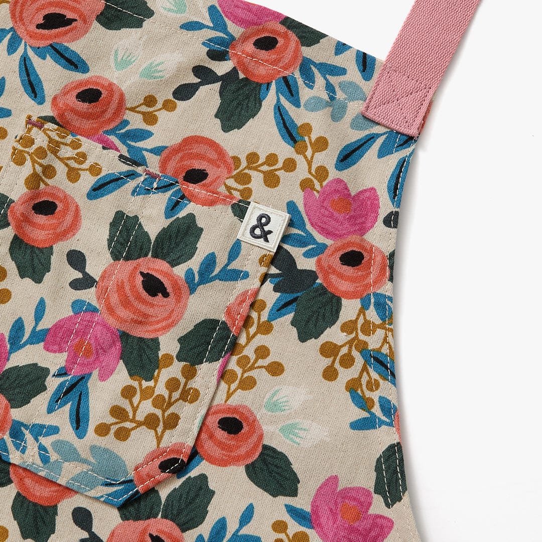 Floral crossback apron close-up with stitched pink strap and small fabric label.