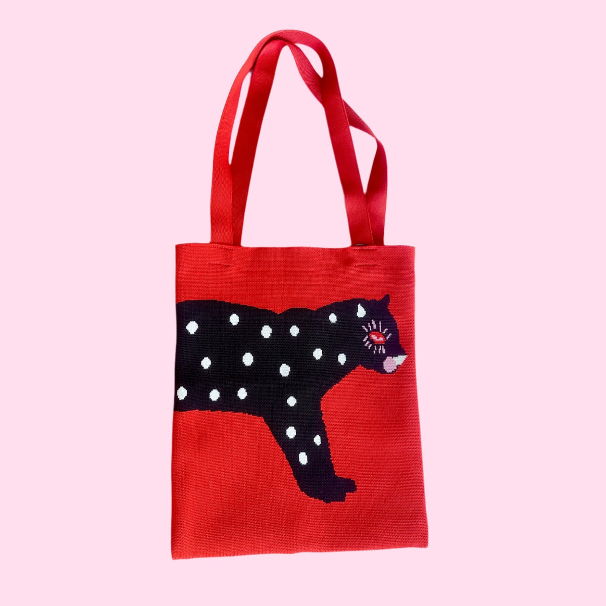 Red knit tote bag with black polka-dot cat graphic and long matching handles.