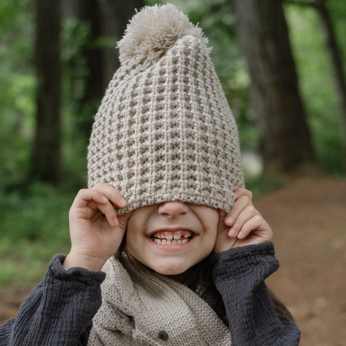 Beige textured pom-pom beanie worn low over a child's eyes