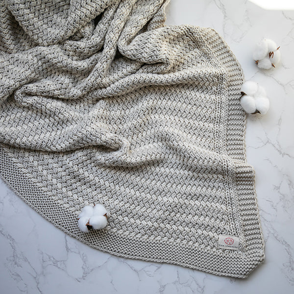 Light gray knit throw blanket with ribbed texture and small logo patch