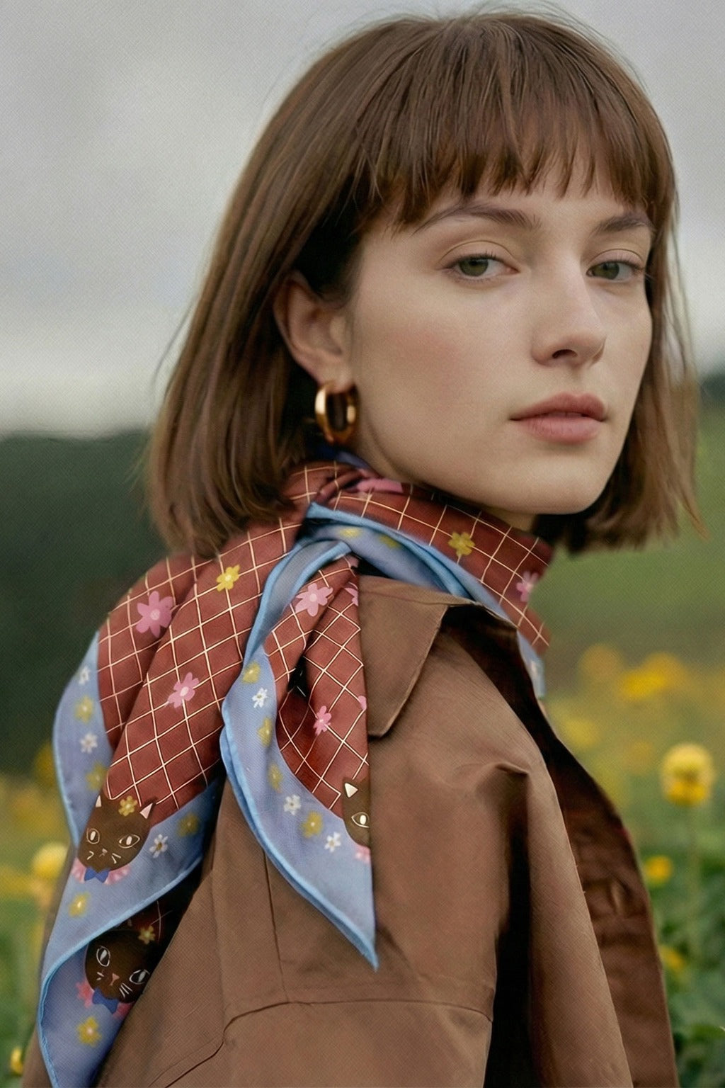 Silk square scarf worn at neck, blue-trimmed brown grid with flower and cat motifs