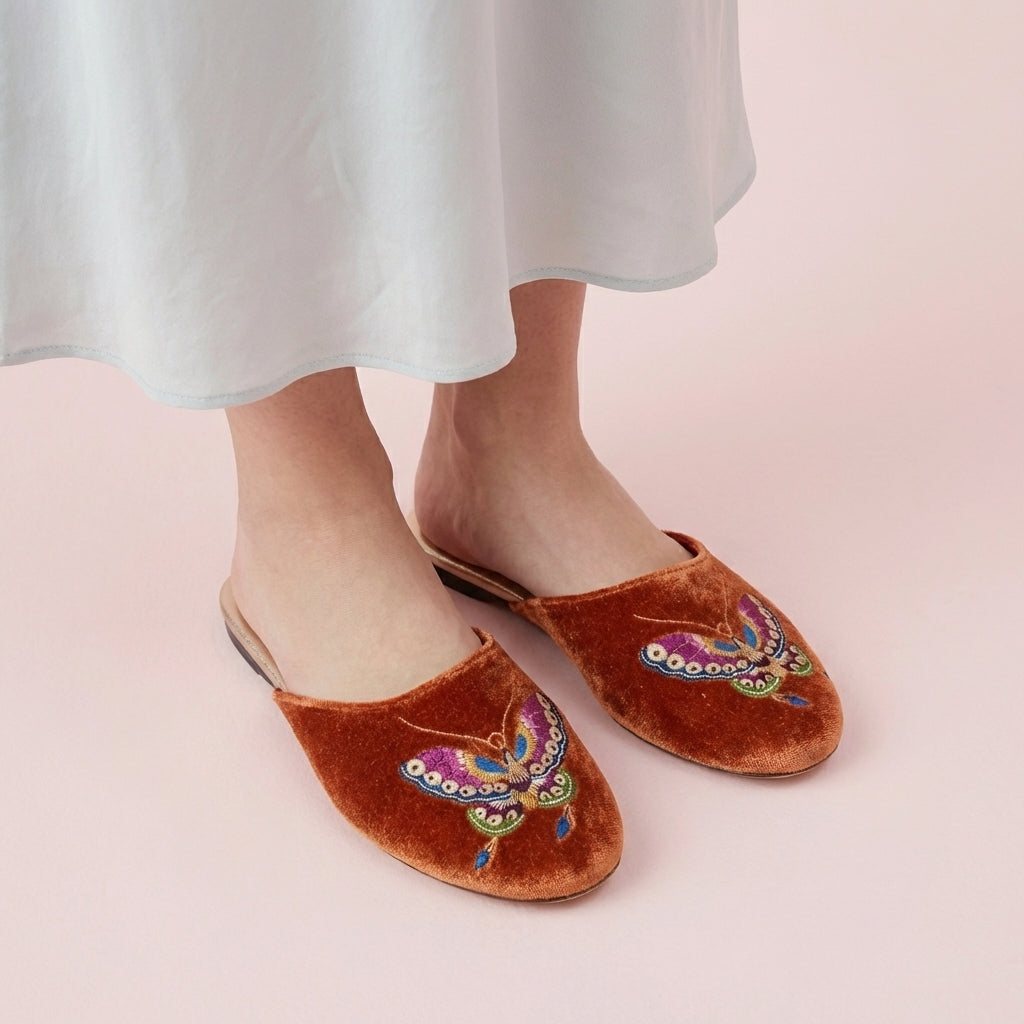 Burnt orange velvet mule slippers with butterfly embroidery, front view pair