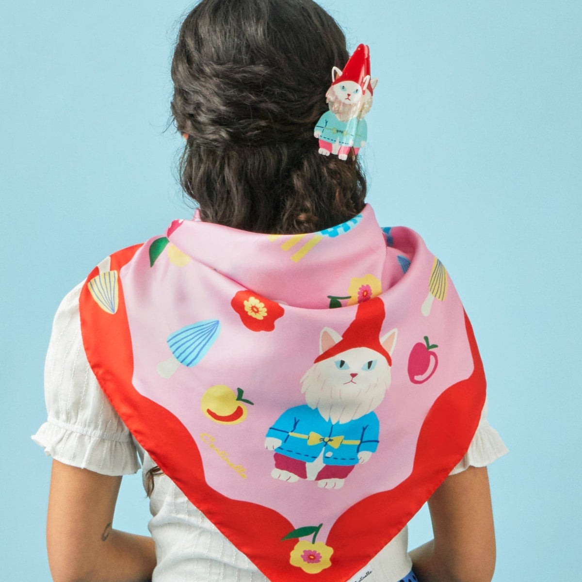 Silk square scarf worn at neck, pink-and-red with cats, flowers, and fruit icons