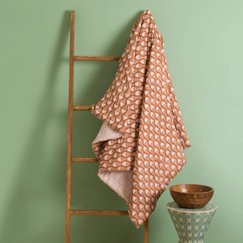 Cotton throw draped on ladder with brown geometric pattern and pink corner fold