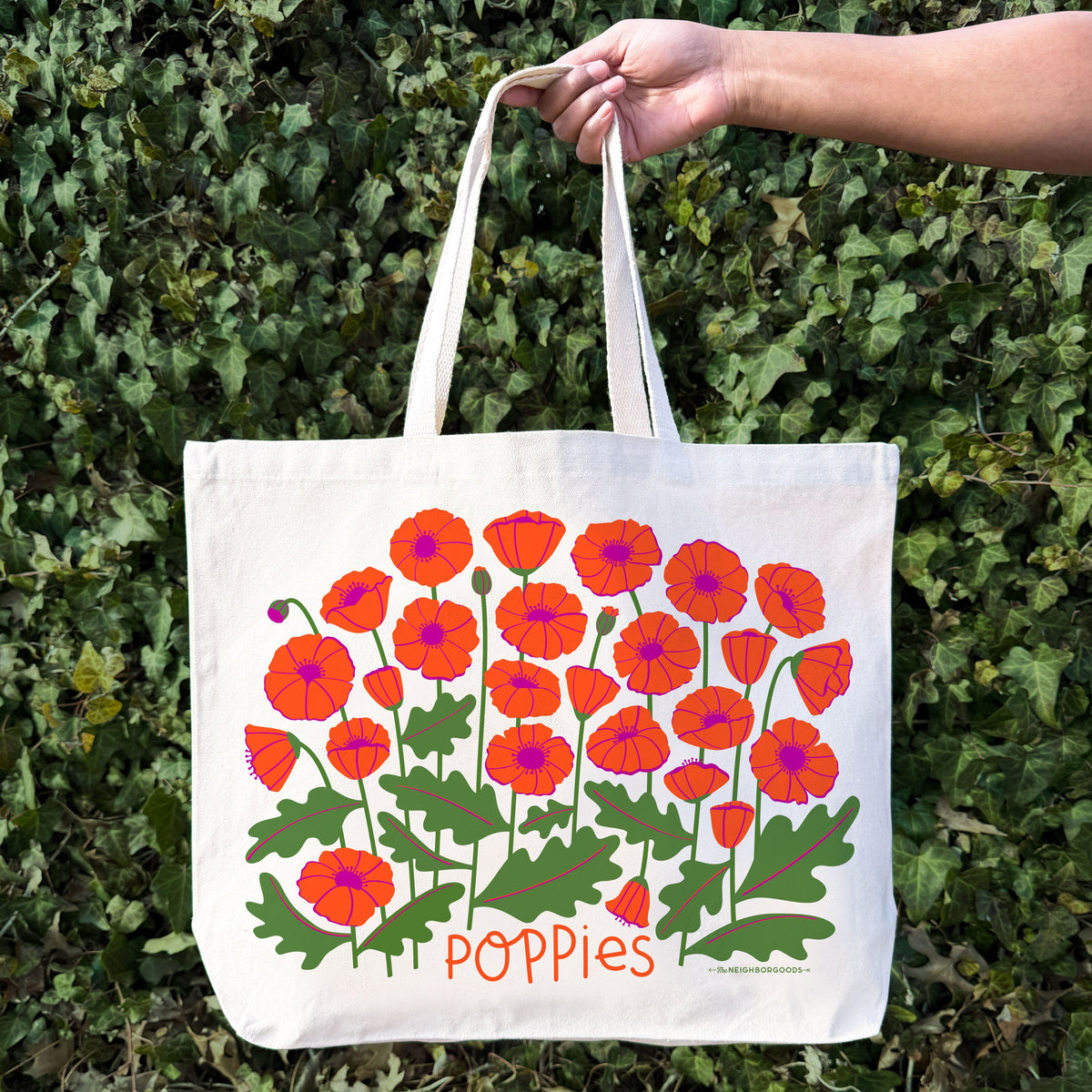White canvas tote bag held in hand with red-orange poppy floral print and “Poppies”.