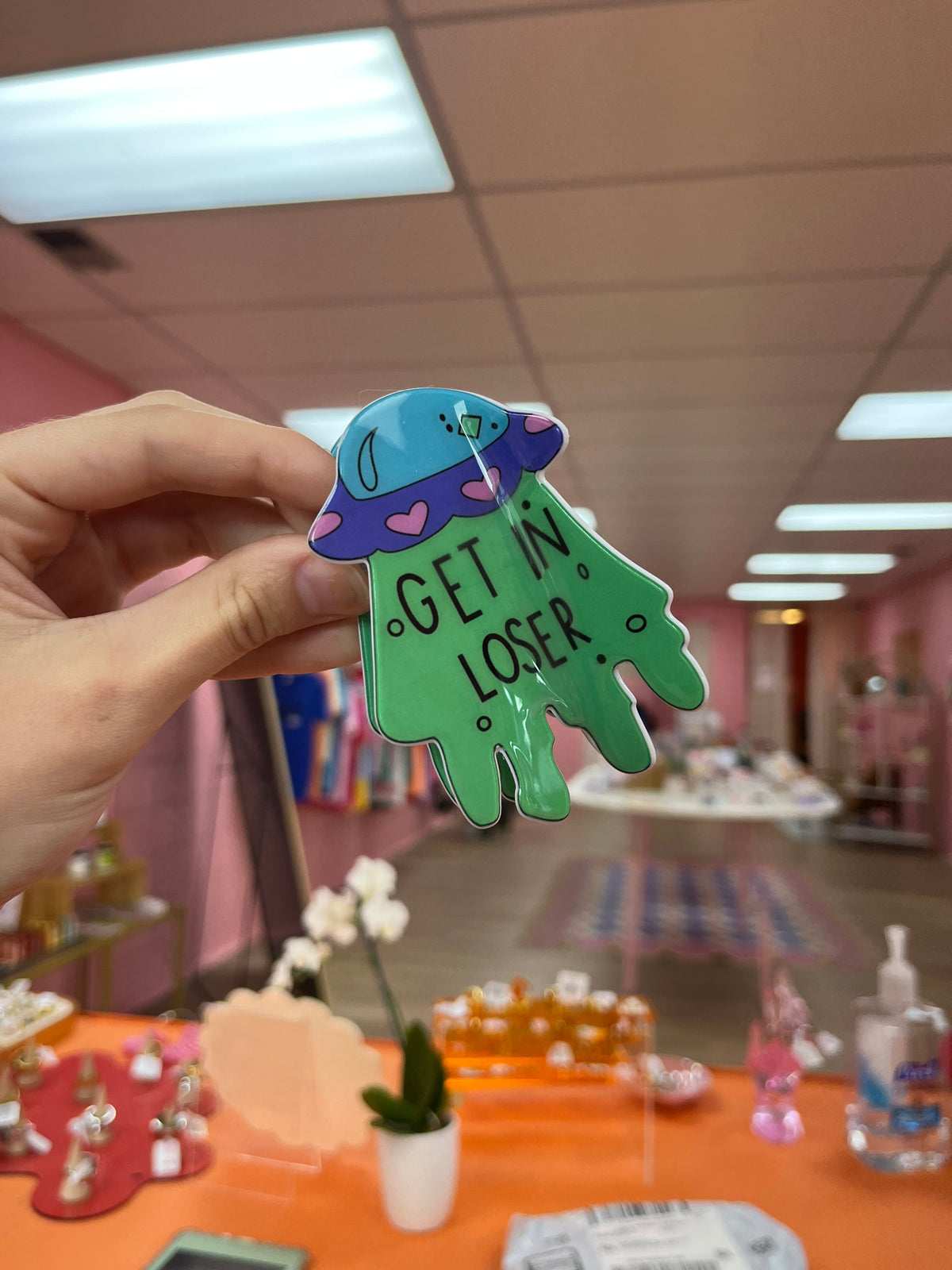 Oopsy Daisy hair claw, green alien with the text “GET IN LOSER”.