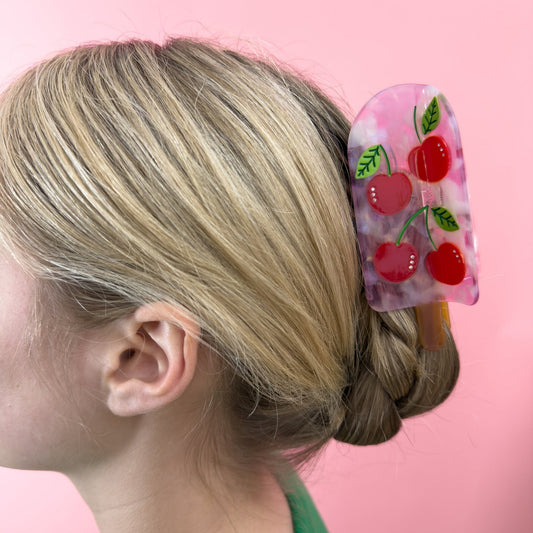 Cherry popsicle hair claw worn on hair; translucent pink clip with red cherry fruit design