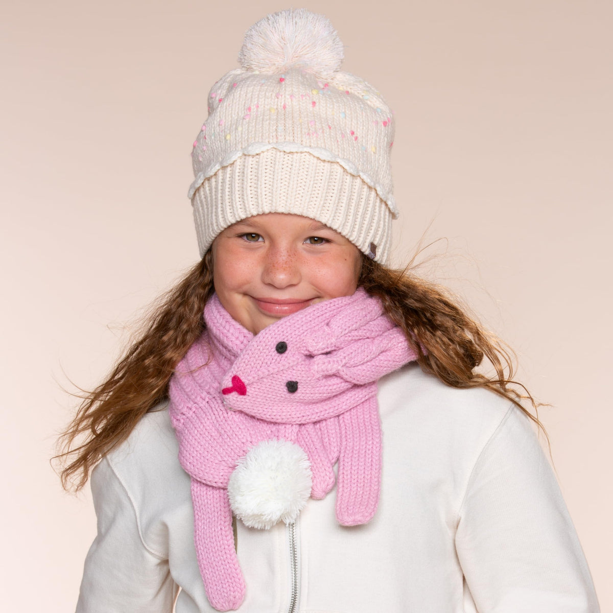 Child wearing a pale speckled knit beanie with ribbed cuff and pom-pom