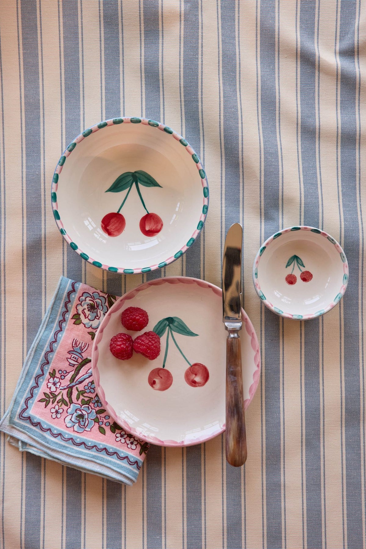 Ceramic cake plate with painted cherries and pink rim, shown with small matching bowl